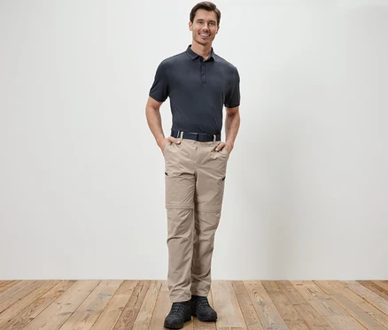 Ein Mann steht mit den Händen in den Taschen einer beige 2-in-1-Funktionshose.