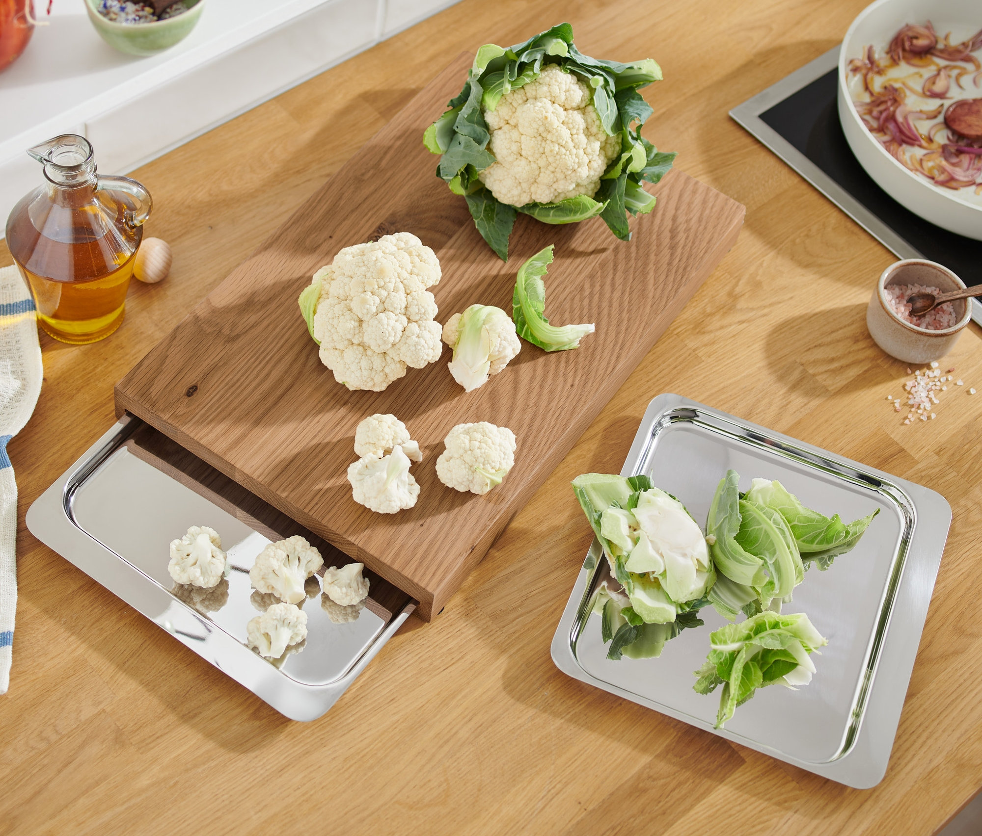 Blumenkohl und geschnittene Stücke auf Schneidebrett und Edelstahltabletts.