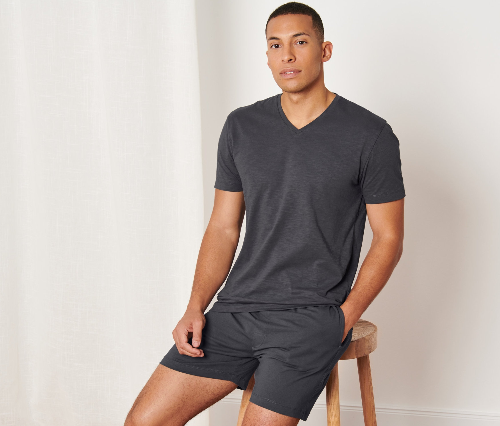 Mann sitzt auf einem Hocker und trägt einen anthrazitfarbenen Shorty-Pyjama.