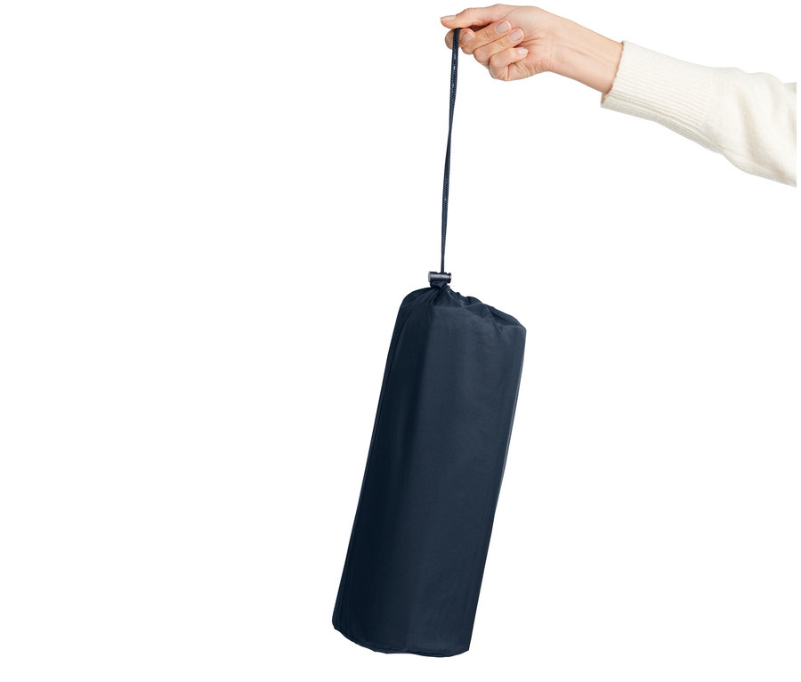 Eine Hand hält eine zusammengerollte Luftmatratze mit integrierter Fußpumpe an einer Schnur.