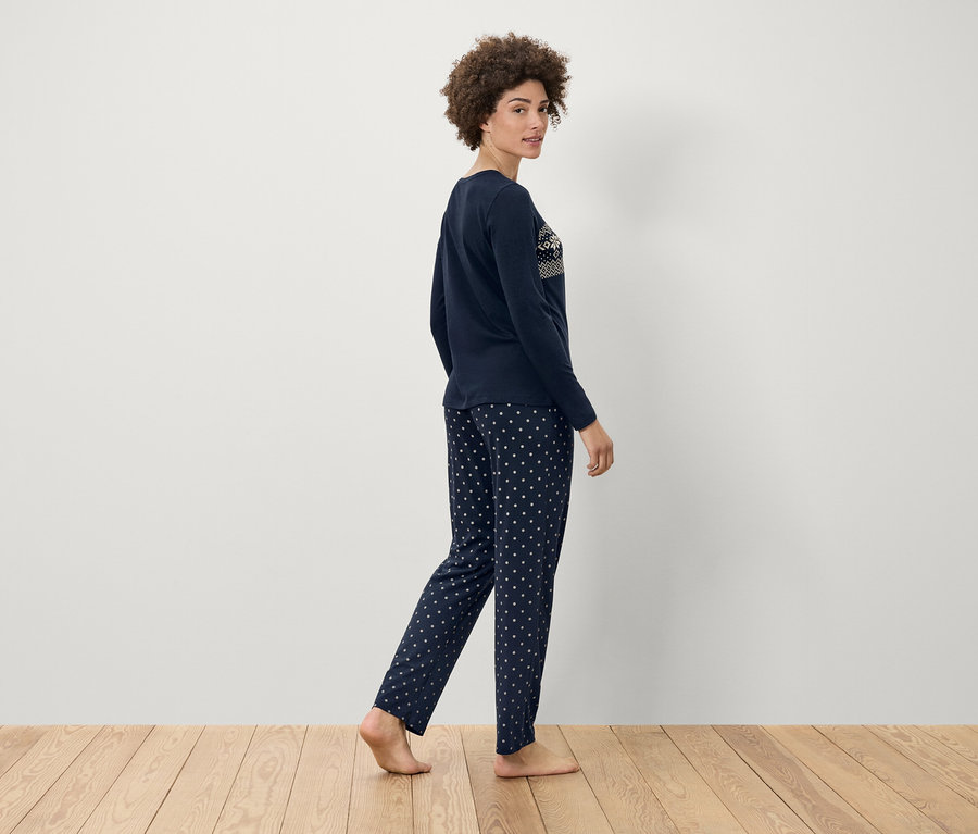 Frau geht in marineblauem Pyjama mit weißen Punkten auf Holzboden.