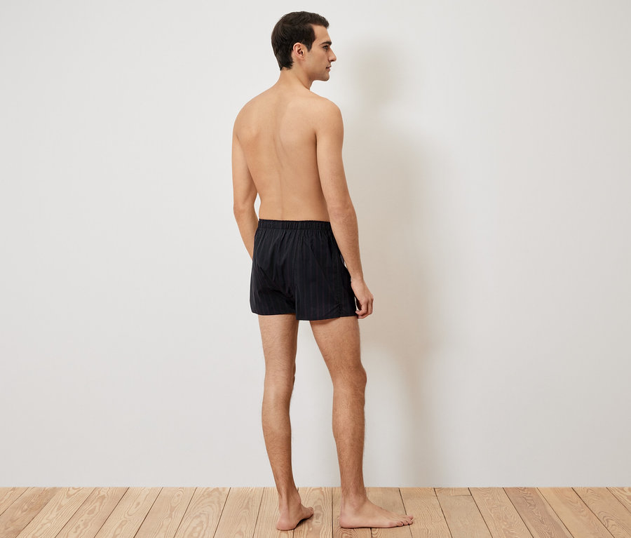 Mann von hinten, trägt schwarze Boxershorts auf Holzboden.