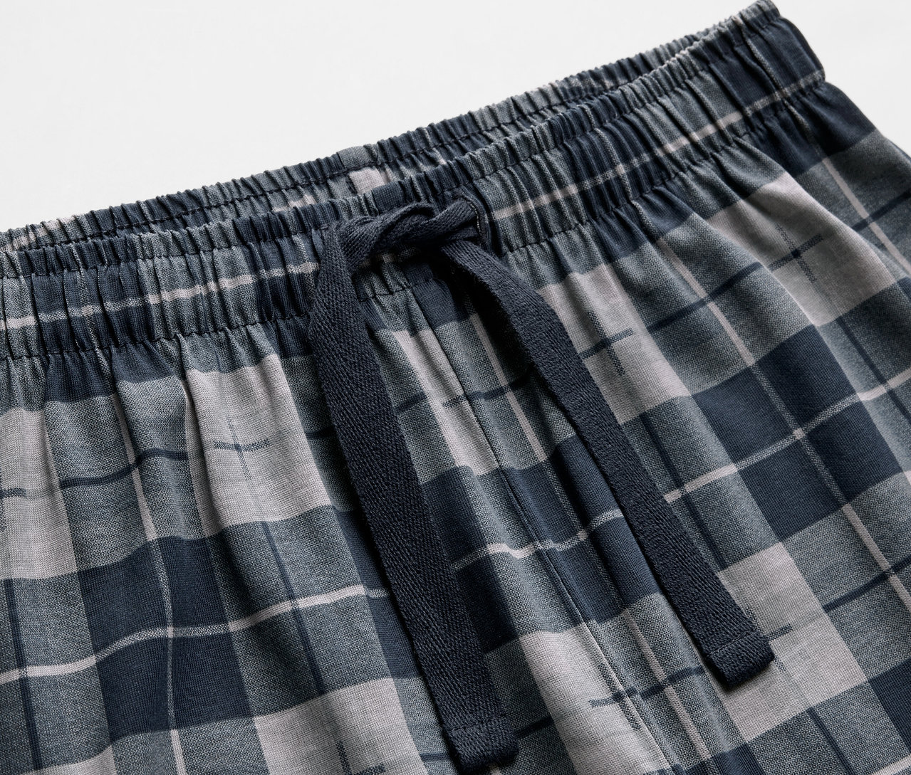 Detailansicht von 2 Kinder-Pyjamas mit blau-grauem Karomuster und Kordelzug.