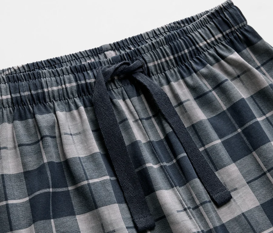 Detailansicht von 2 Kinder-Pyjamas mit blau-grauem Karomuster und Kordelzug.