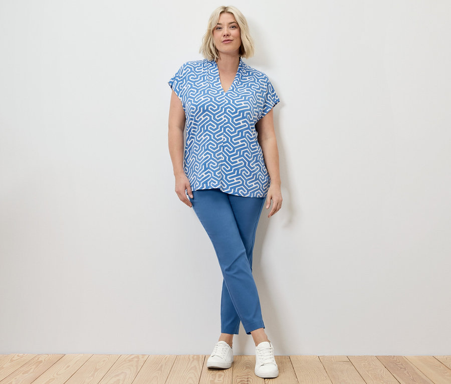 Blonde Frau posiert in blauer Stretchhose und blauem Blusenshirt mit V-Ausschnitt.