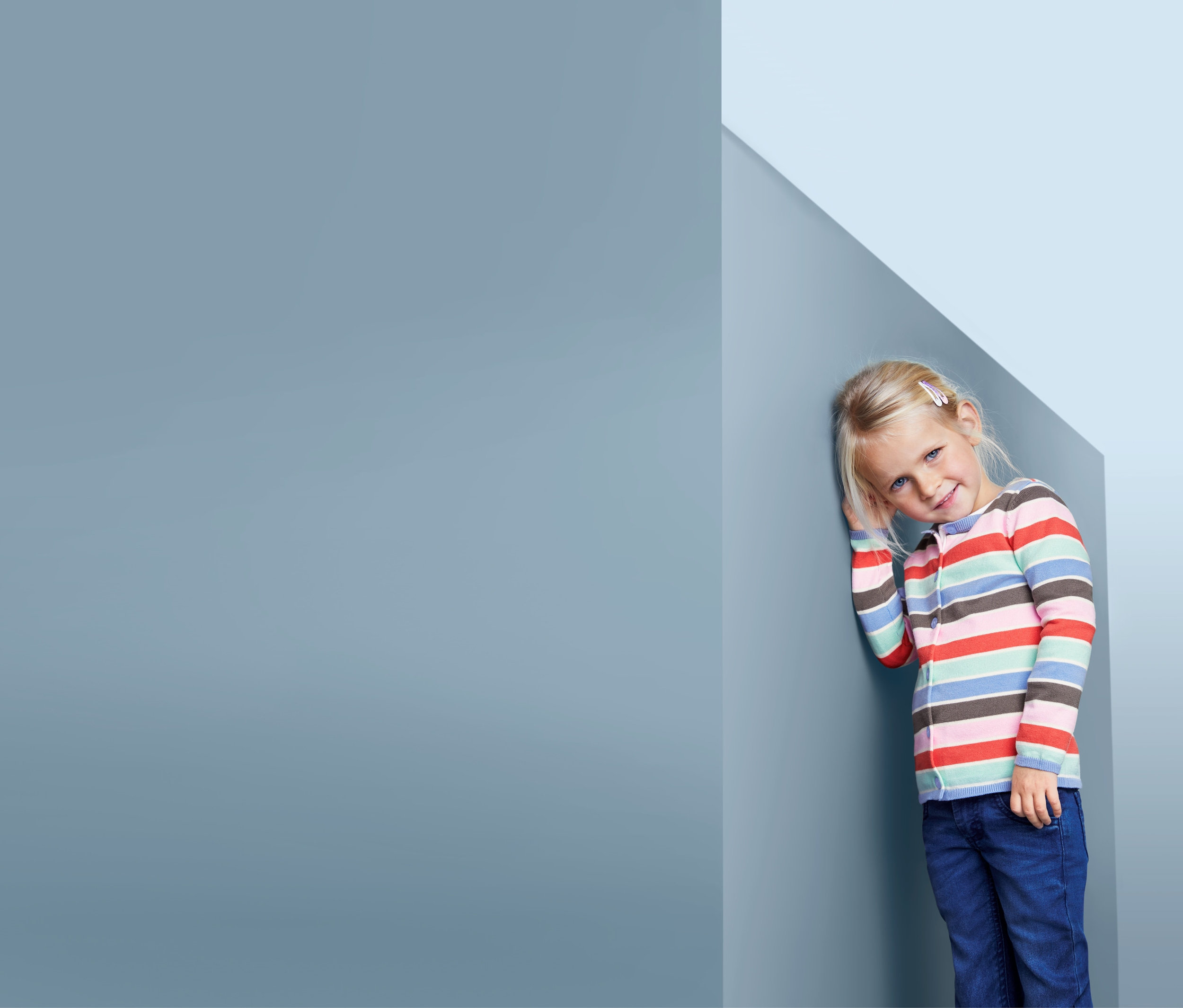 Mädchen lehnt an einer Wand und trägt eine gestreifte Strickjacke.