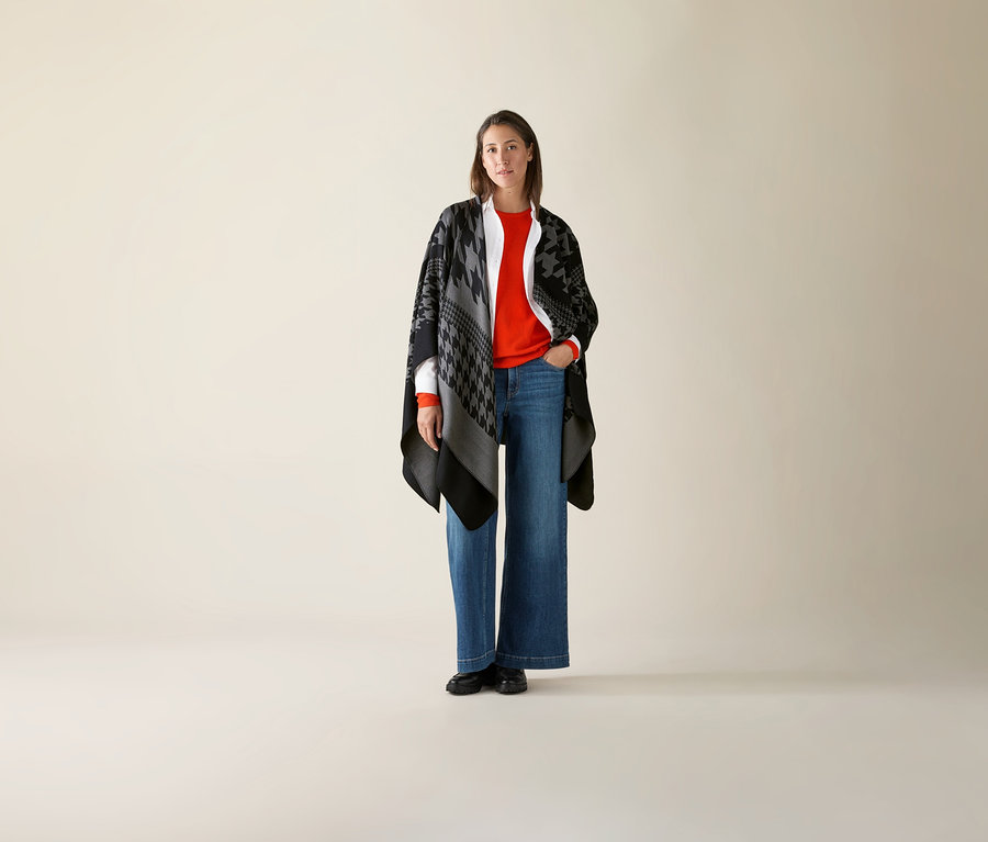 Frau steht und trägt einen orangen Mernio-Feinstrickpullover.