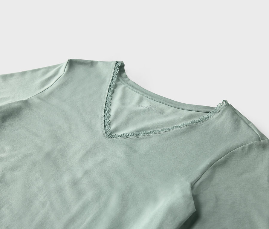 Detailansicht eines hellgrünen T-Shirts mit kurzen Ärmeln und V-Ausschnitt, der mit Spitze verziert ist.