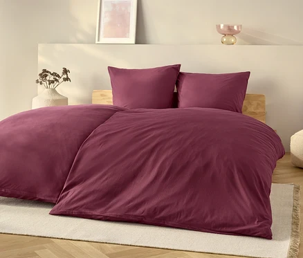 Ein lila Bettwäsche-Set auf einem Bett mit einem weißen Teppich.