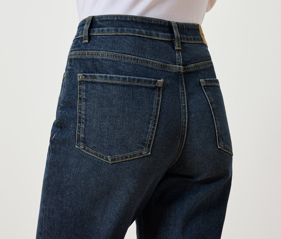 Detailansicht der Rückseite von dunkelblauen Jeans an einer Person vor einem weißen Hintergrund.