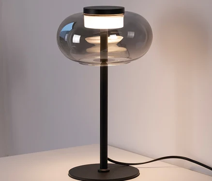 Eine graue Tischleuchte mit Glasschirm steht auf einem weißen Tisch.