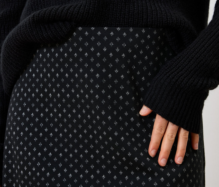 Detailaufnahme eines schwarzen Damenrocks mit kleinem Muster und eines schwarzen Pullovers.