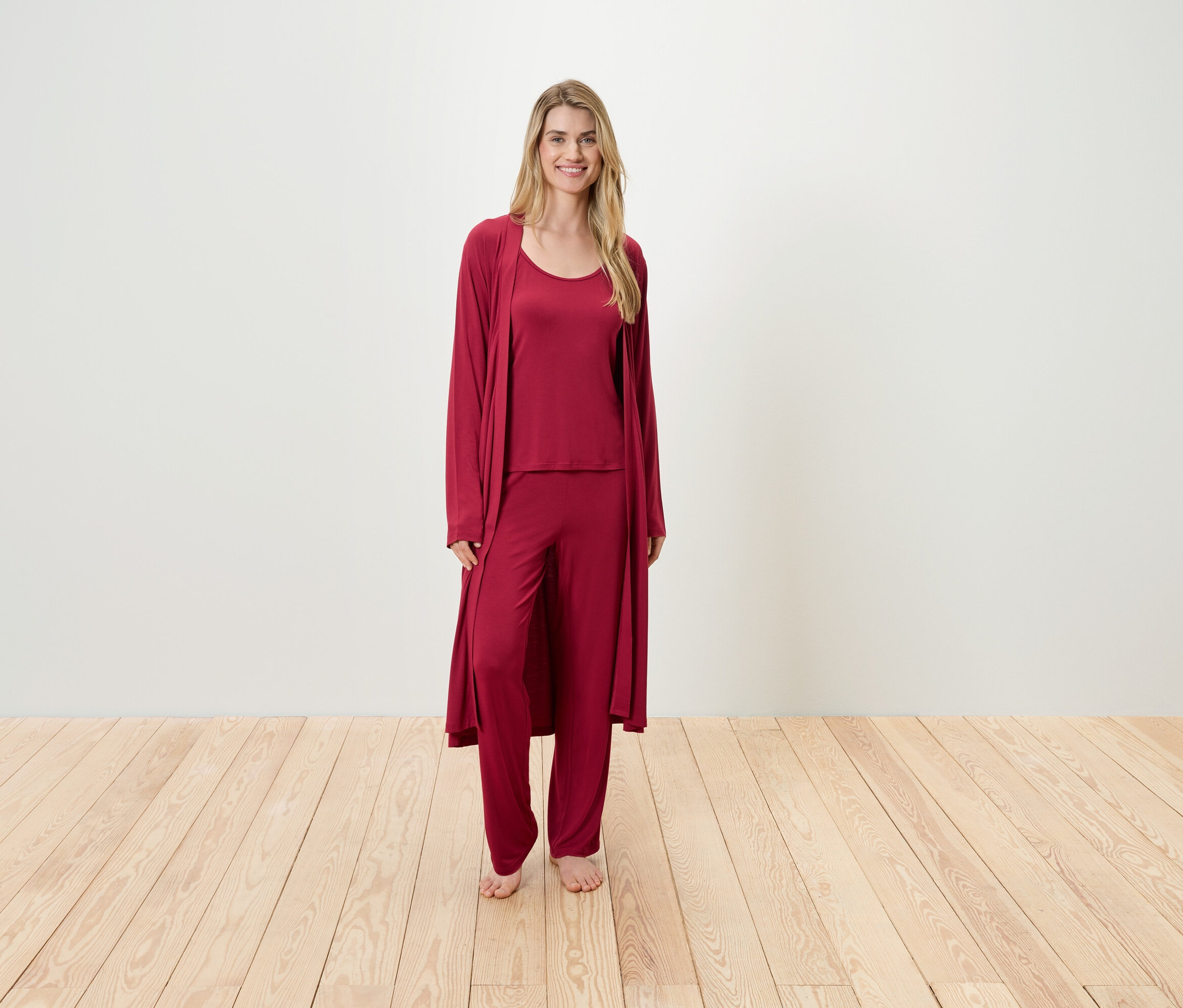 Eine Frau steht und trägt einen weinroten Schlafanzug, der aus einem Tanktop, einer Hose und einem Morgenmantel besteht.