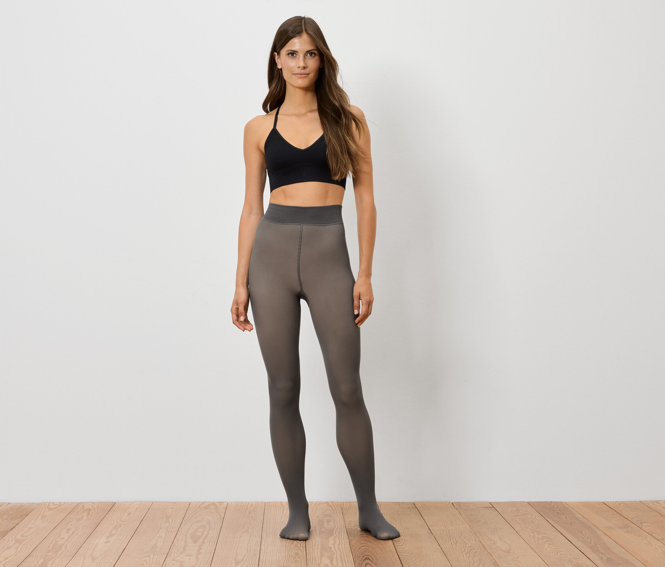 Frau steht und trägt ein schwarzes Sportoberteil und graue Strumpfhose.