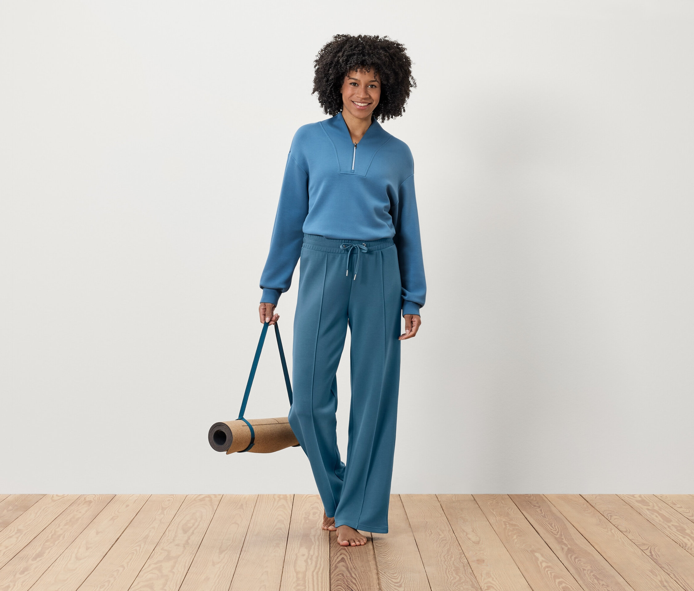 Frau im blauen Trainingsanzug hält eine Yogamatte.