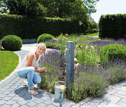 Blonde Frau in Jeans kniet an Lavendel in der Nähe von Garantia Wassersäule, Granit