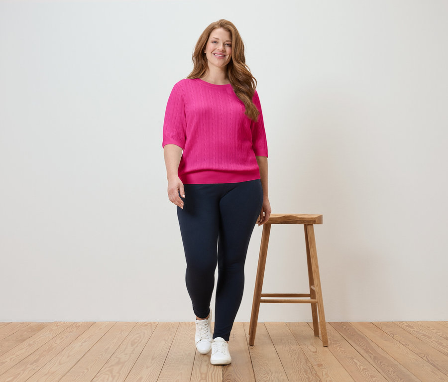 Frau geht in pinkfarbenem Oberteil und marineblauer Leggings auf Holzboden