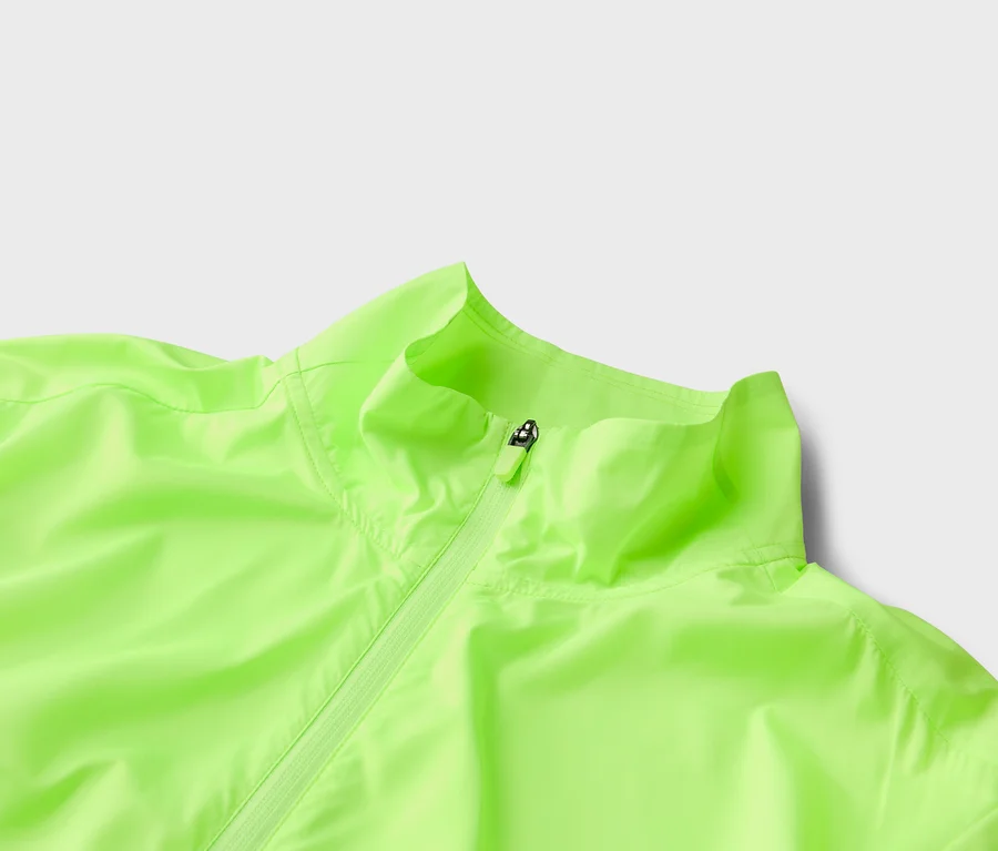 Nahaufnahme einer hellgrünen Jacke mit Reißverschluss und Kragen vor einem hellgrauen Hintergrund.