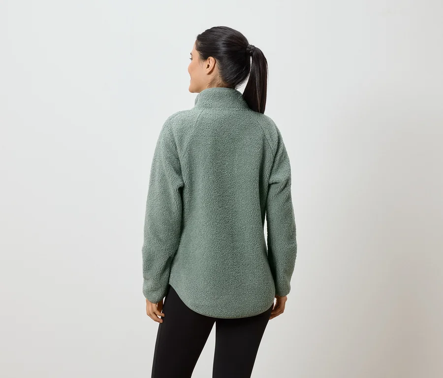 Eine Frau mit Pferdeschwanz trägt einen mintgrünen Fleecepullover und schwarze Leggings, von hinten gesehen.