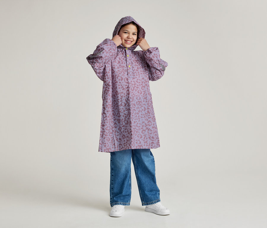 Ein lächelndes Mädchen mit Kapuze trägt einen lila Regenmantel mit Leopardenmuster und blaue Jeans.