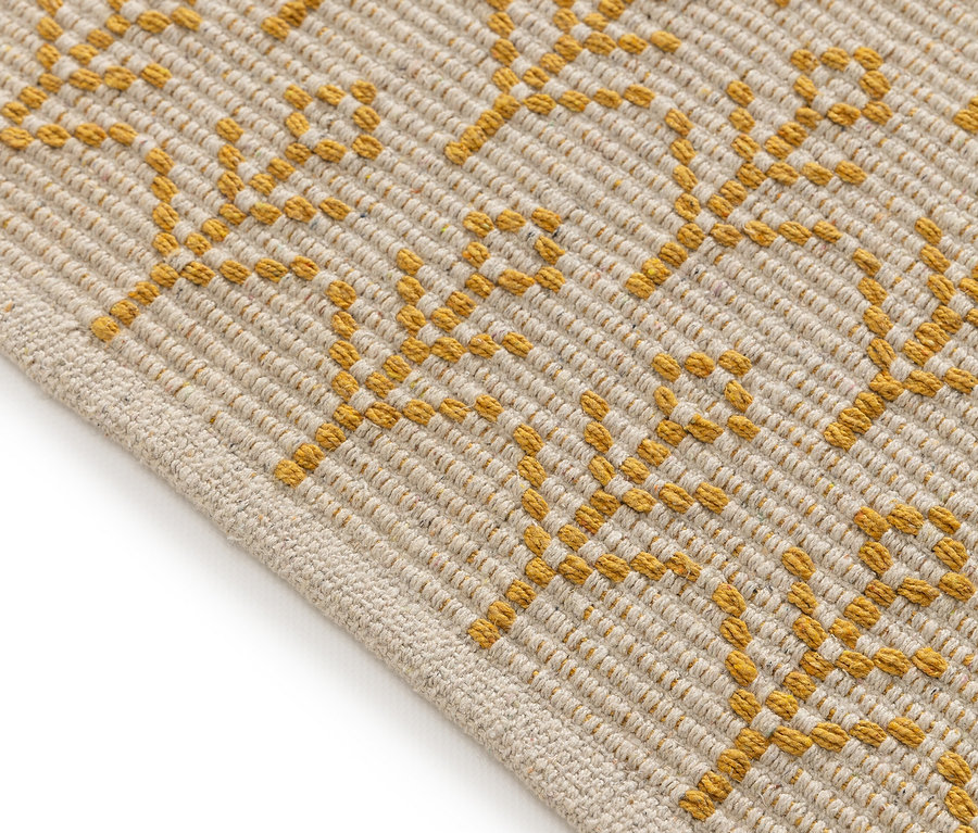 Nahaufnahme einer beigen Teppich Ecke mit goldfarbenem Muster.