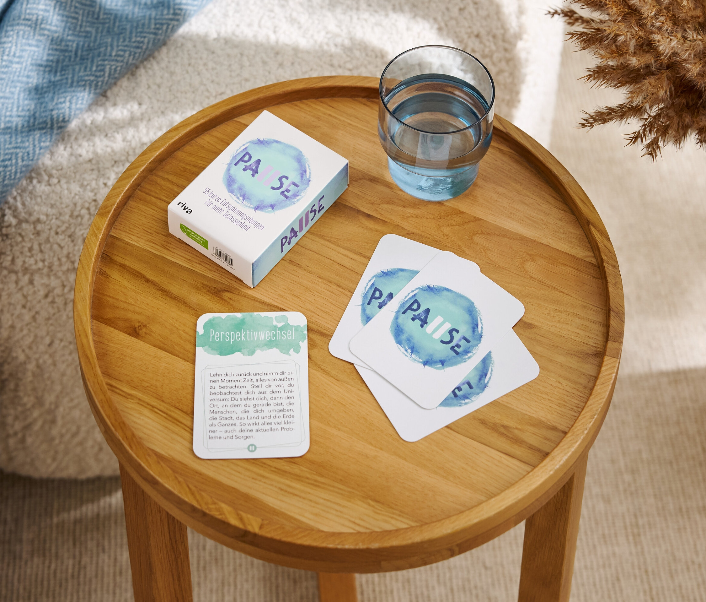 Auf einem runden Holztisch liegen eine Schachtel und Karten mit der Aufschrift "PAUSE" sowie ein Glas Wasser.