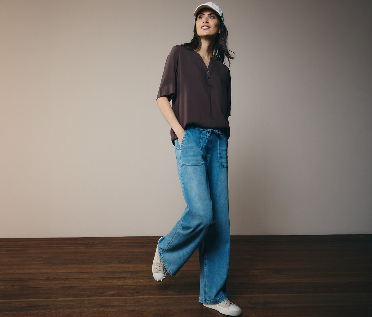 Frau mit Basecap und brauner CECIL Tunikabluse zu Jeans und Turnschuhen.