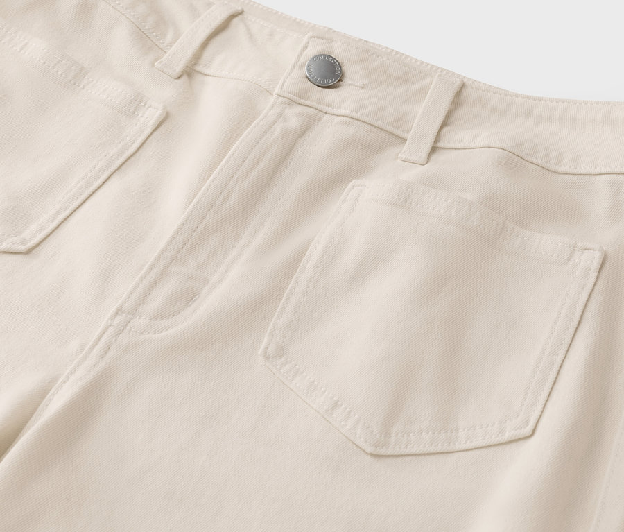 Detailaufnahme von hellbeigen Jeans mit Taschen und einem silberfarbenen Knopf.