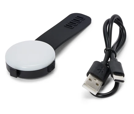Ein schwarzes, rundes LED-Licht mit einem schwarzen Griff und einem USB-Kabel liegt auf einem weißen Hintergrund.