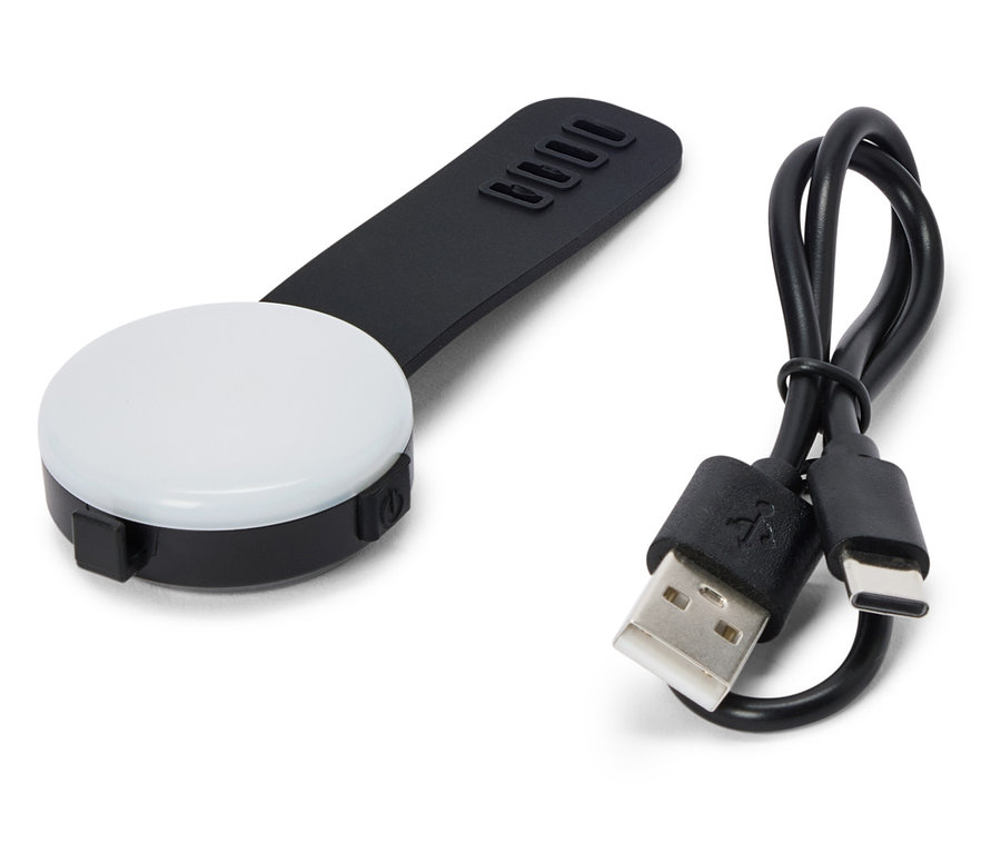 Ein schwarzes, rundes LED-Licht mit einem schwarzen Griff und einem USB-Kabel liegt auf einem weißen Hintergrund.