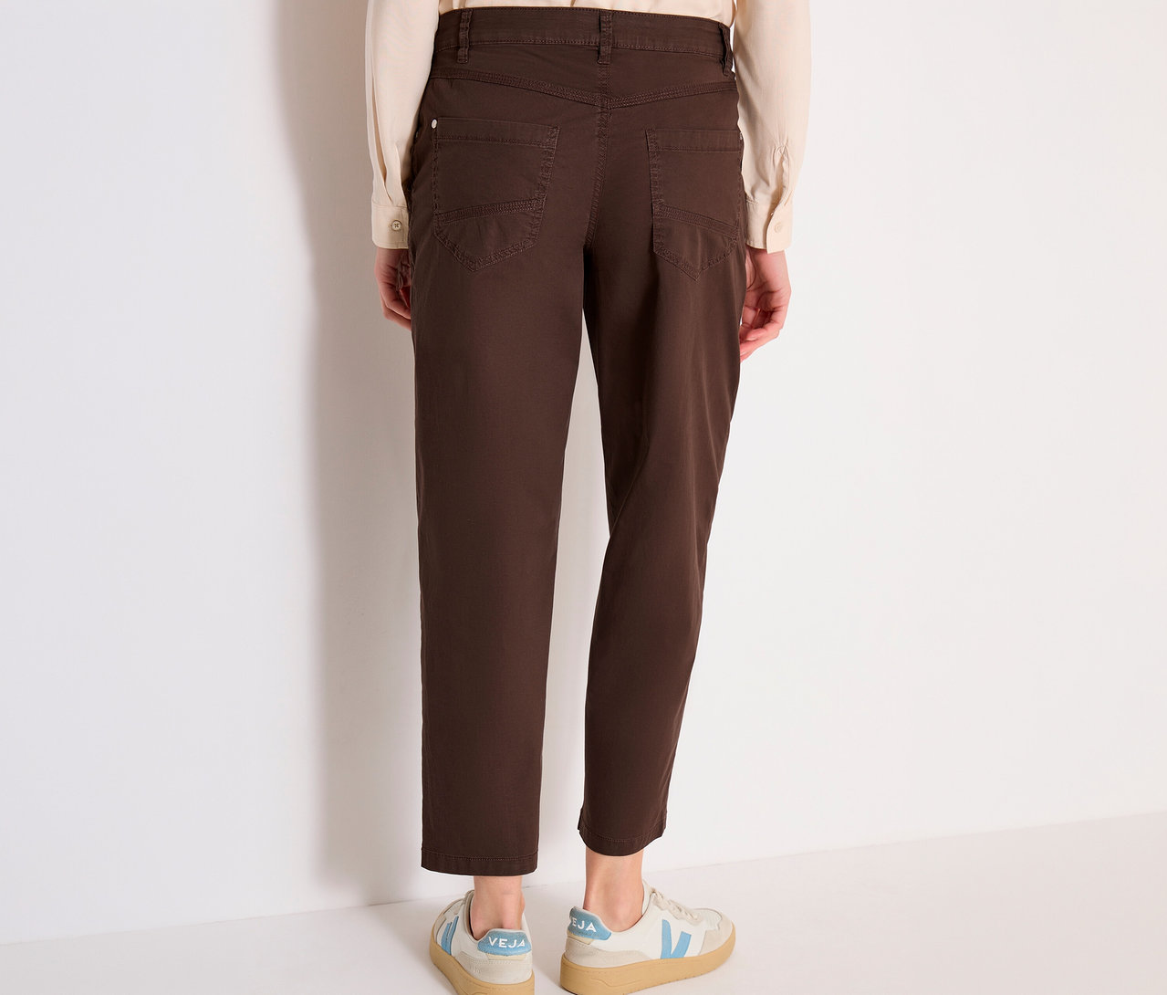 Eine Person steht mit dem Rücken zur Kamera, trägt ein helles Hemd, eine braune CECIL Barrel »Scarlett« Hose und helle Sneaker.