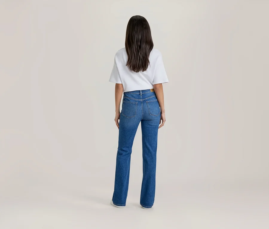 Frau steht mit dem Rücken zum Betrachter, trägt ein weißes Kurzarm-T-Shirt und eine blaue High-Waist-Jeans.