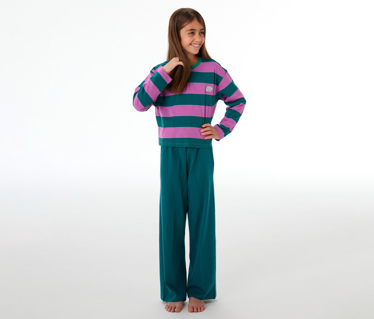 Lächelndes Mädchen in einem SCHIESSER Kinder-Pyjama mit lila-grün gestreiftem Oberteil und grüner Hose.