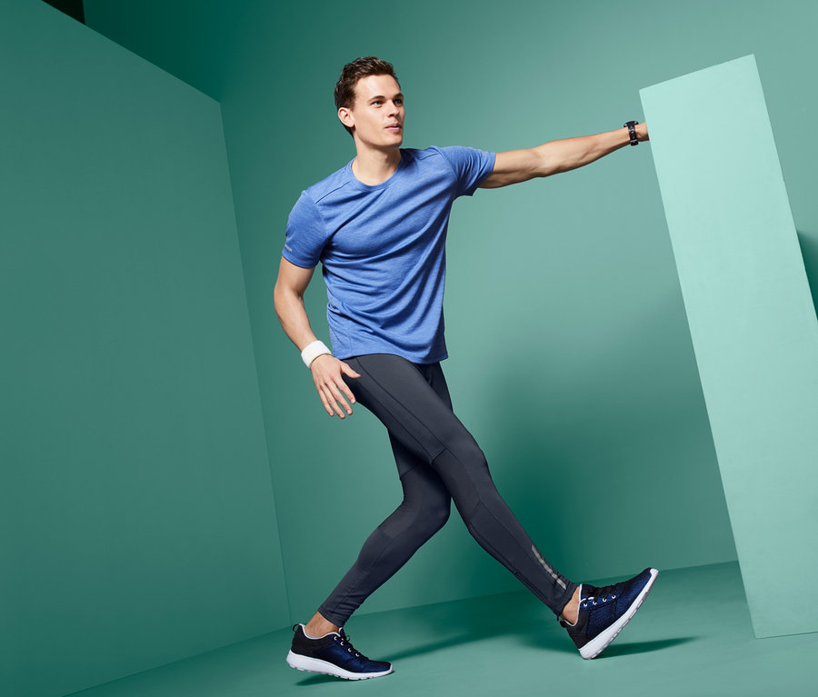 Mann in blauem T-Shirt und Lauftight posiert neben einer grünen Wand.