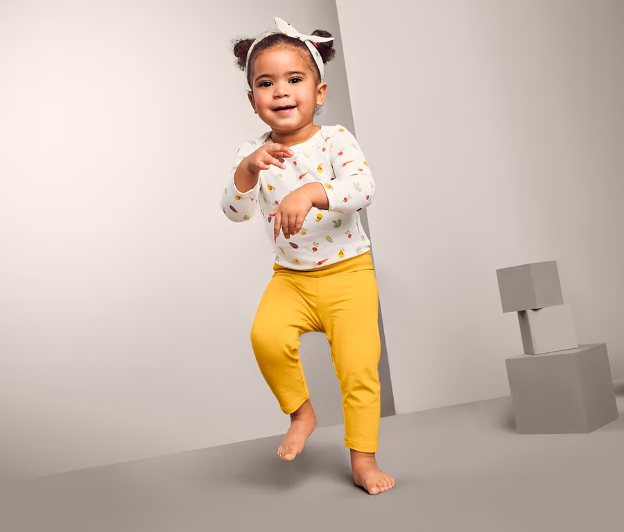 Lächelndes kleines Mädchen tanzt und trägt eine 3-teilige Baby-Kombi.
