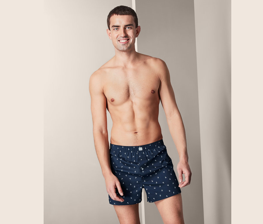 Lächelnder Mann trägt 2 Web-Boxershorts mit Ankerdruck.