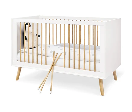 Weißes Pinolino Babybett »Edge« mit Holzstäben und einem Plüschpinguin darin.