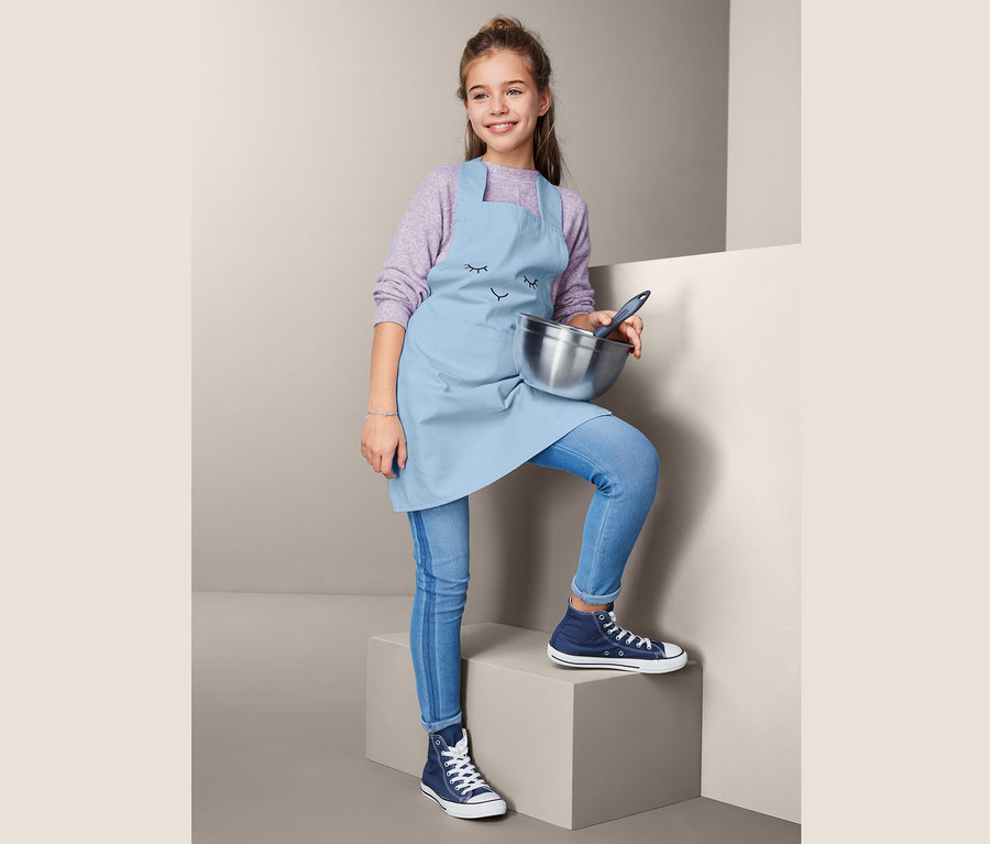 Mädchen mit Kinder-Küchenschürze hält Schüssel.