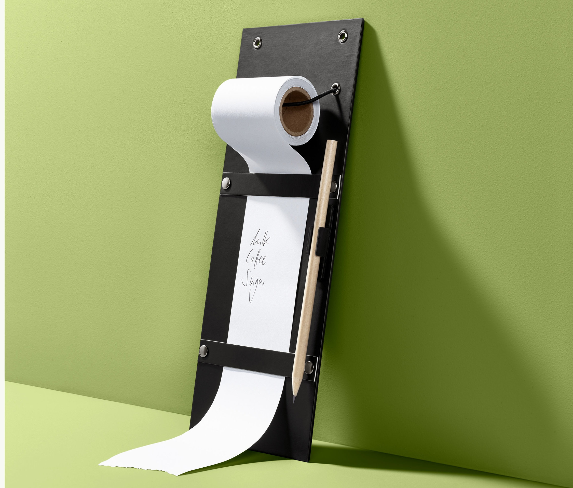 Ein Notizrollenhalter in Schwarz mit Papierrolle, Bleistift und der Aufschrift Milch, Kaffee, Zucker.