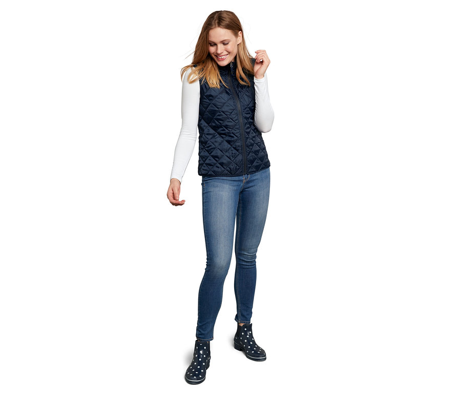 Frau trägt eine gesteppte Weste und Jeans mit Regenboots.