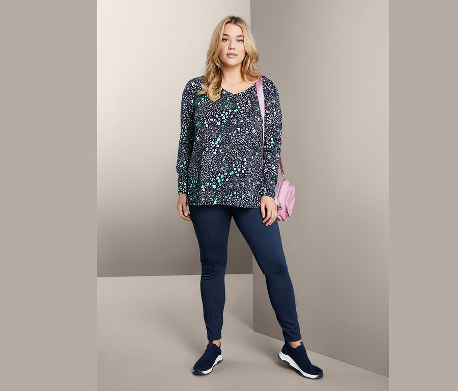 Frau posiert in Langarmshirt, Bodyforming-Jerseyhose, Slip-on-Sneaker und Umhängetasche.