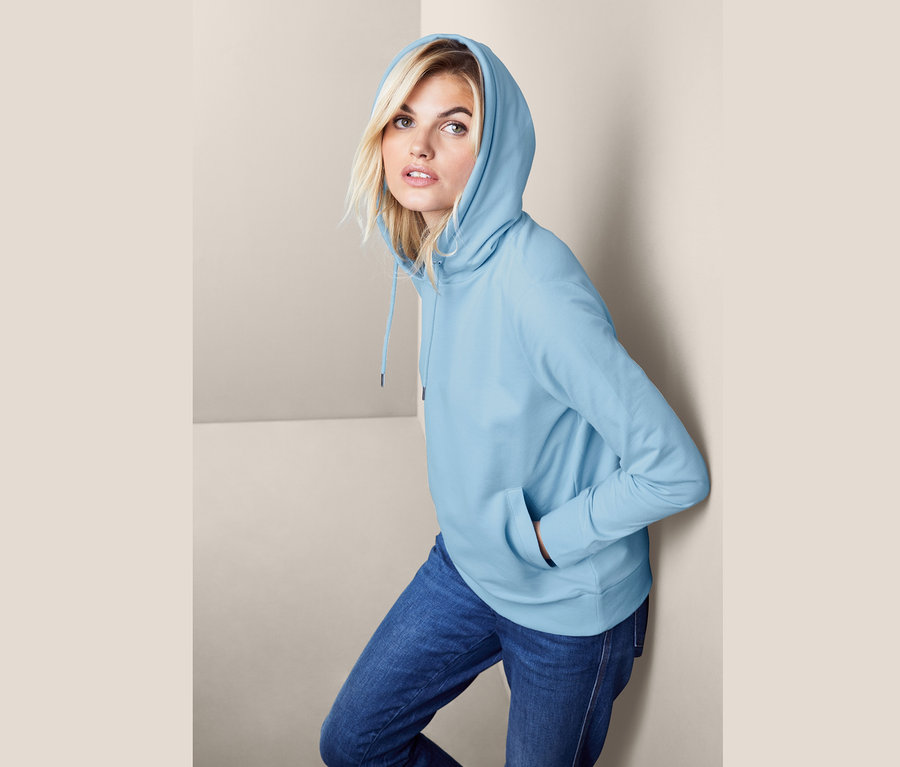 Frau posiert in hellblauem Kapuzensweatshirt.