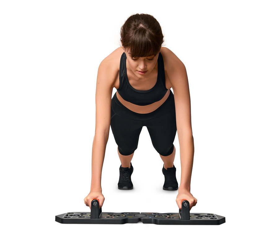 Frau macht Liegestütze auf einem Liegestütz-Board mit Elastikbändern.