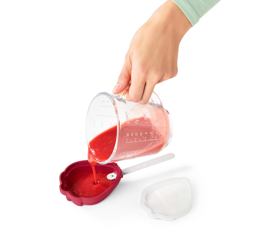 Eine Person gießt rote Flüssigkeit aus einem Messbecher in eine rote Eisform aus einem 4er-Set.