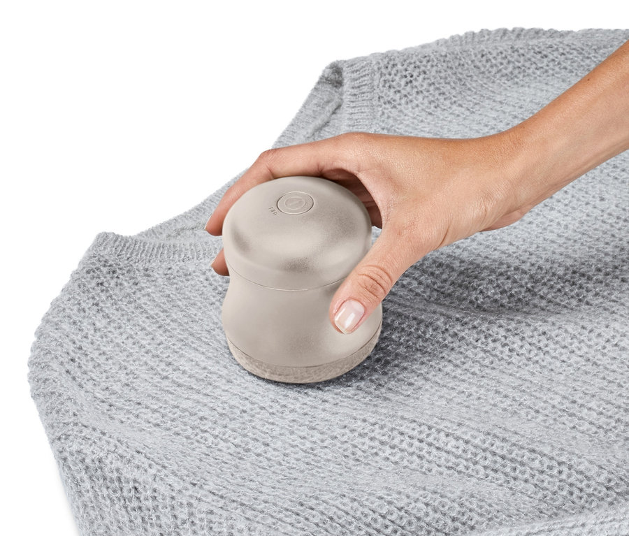 Eine Hand benutzt einen Fusselrasierer auf einem grauen Pullover.