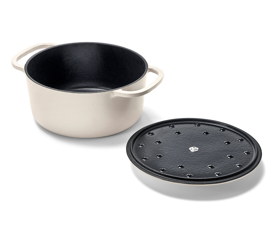 Ein cremefarbener Gusseisen-Bräter und sein Deckel liegen nebeneinander.