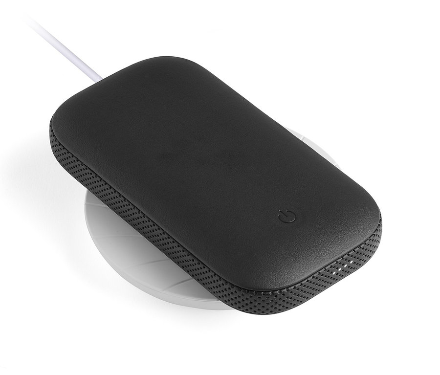 Schwarzer Lexon »POWERSOUND« Lautsprecher inkl. Powerbank auf einer weißen, kabellosen Ladestation.