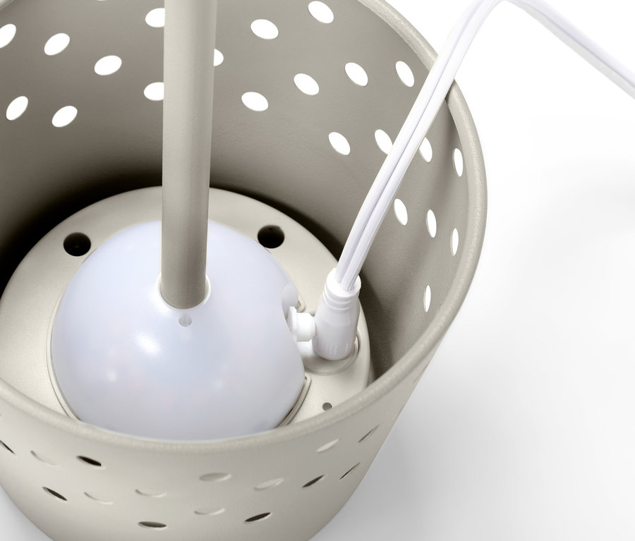 Detailansicht einer grauen LED-Akku-Tischleuchte aus Metall in einem Behälter mit Löchern.