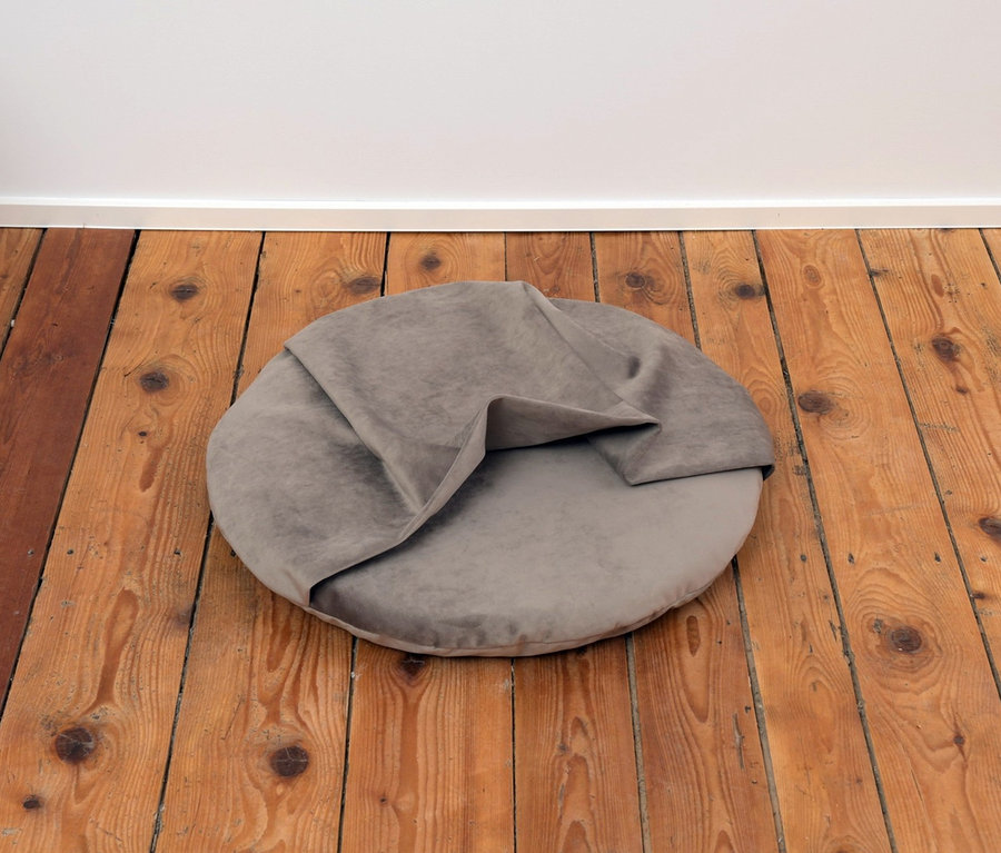 Ein graues Liegekissen »Iglu« liegt auf einem Holzboden.