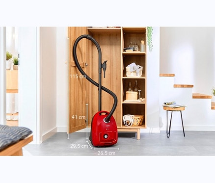 Ein roter Bosch BGD38RD1H Bodenstaubsauger mit Beutel steht vor einem offenen Holzschrank.